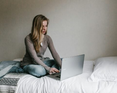 woman typing on MacBook Pro while sitting on bed in room