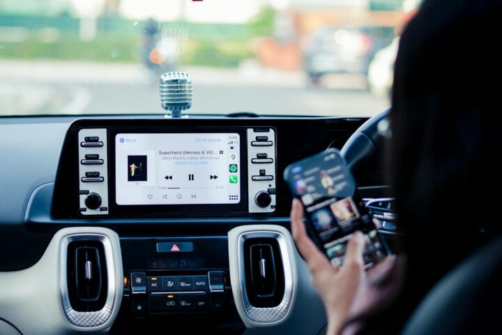 Car dashboard with a touchscreen display and person using a smartphone inside a vehicle.