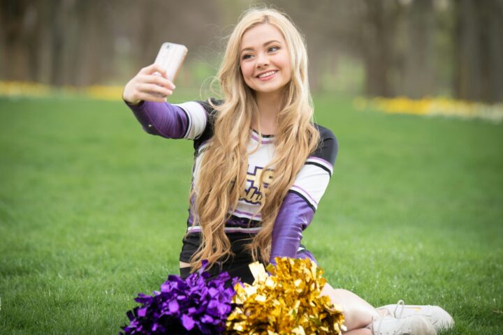 a girl sitting on the grass taking a selfie with her cell phone