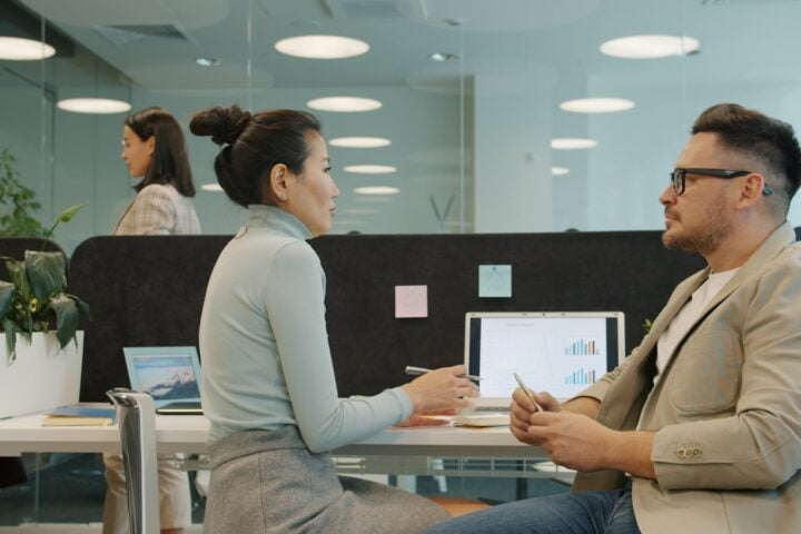 Two colleagues discussing work at their desks.