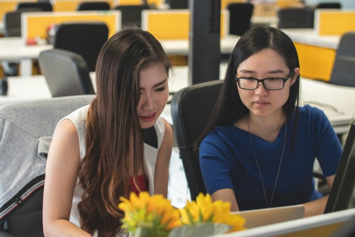 two sitting woman looking at silver laptop computer