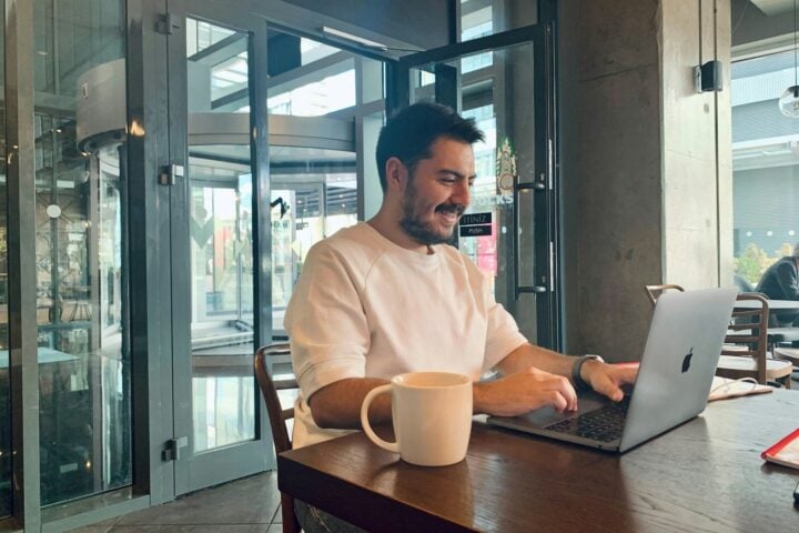 Man smiling while working on laptop in cafe.